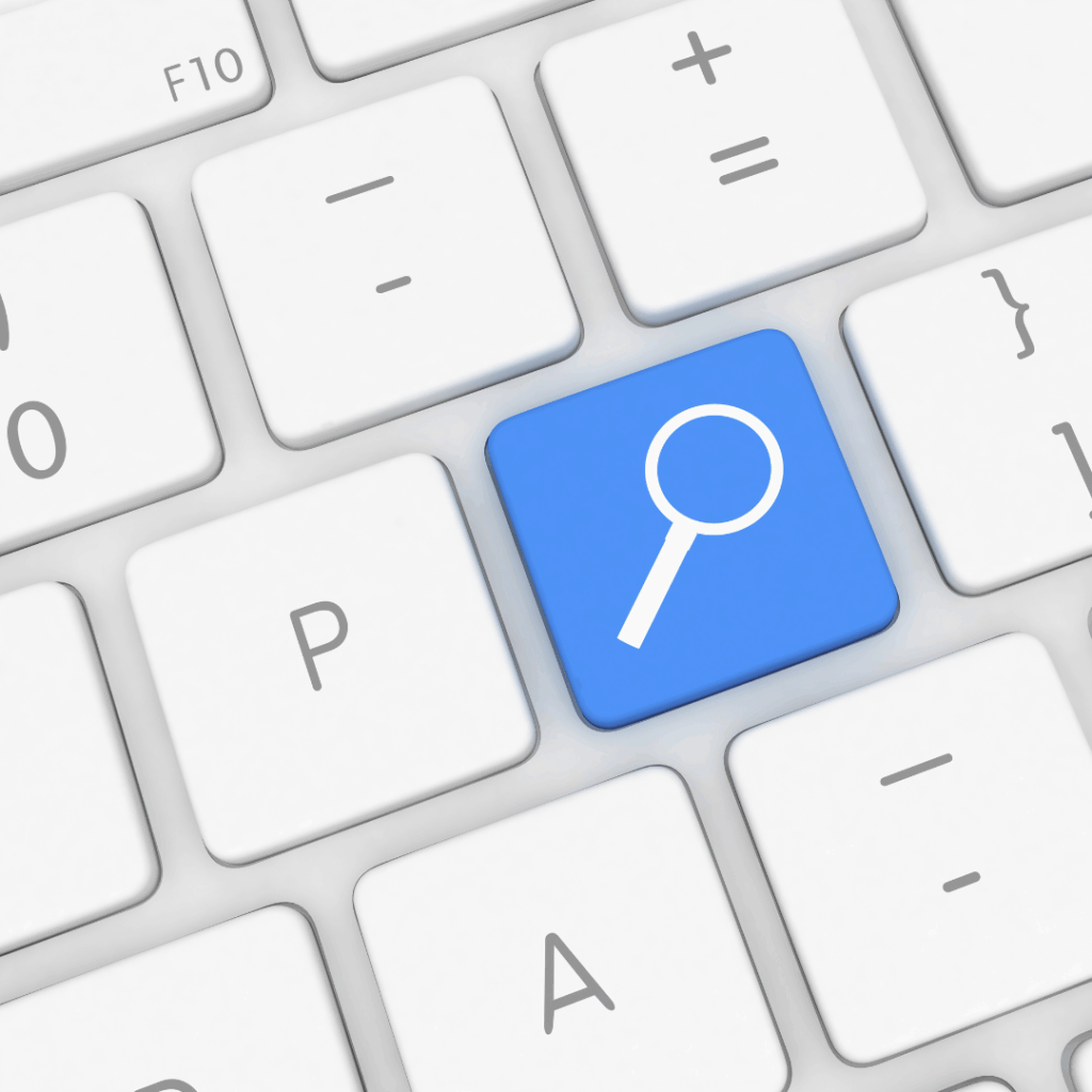 A computer keyboard with a blue key featuring a white magnifying glass icon, symbolizing a search function, surrounded by standard white letter and symbol keys.