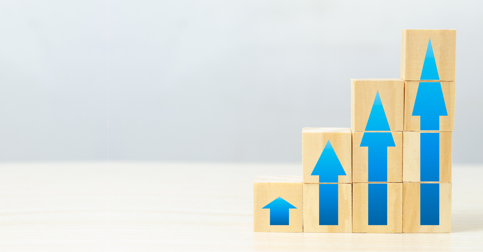 Wooden blocks arranged in a staircase shape, each with a blue upward arrow, symbolize brand and market visibility growth and progress against a light background.